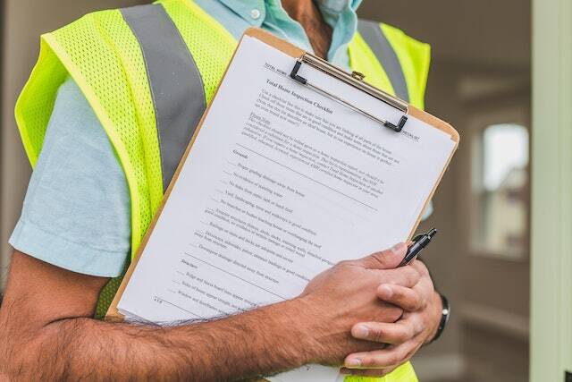 person in yellow reflective vest holding click-board with home inspection checklist